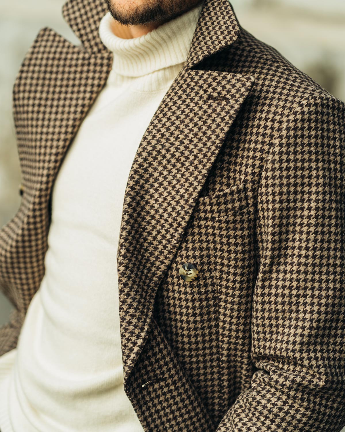 Man wearing a houndstooth patterned coat over a white turtleneck sweater.