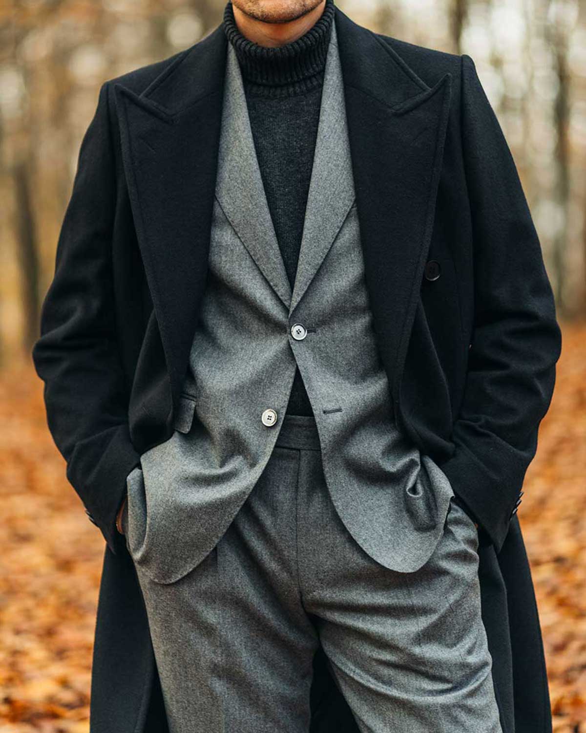 Man wearing a black double breasted coat over a grey flannel suit