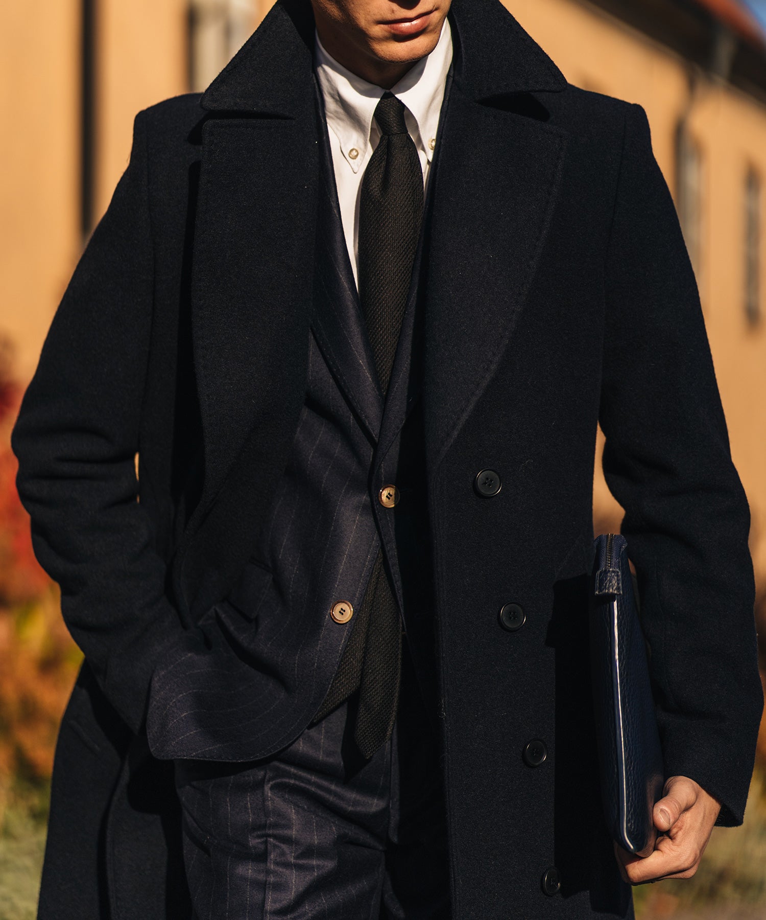 Man wearing a double breasted overcoat over a suit with shirt and tie
