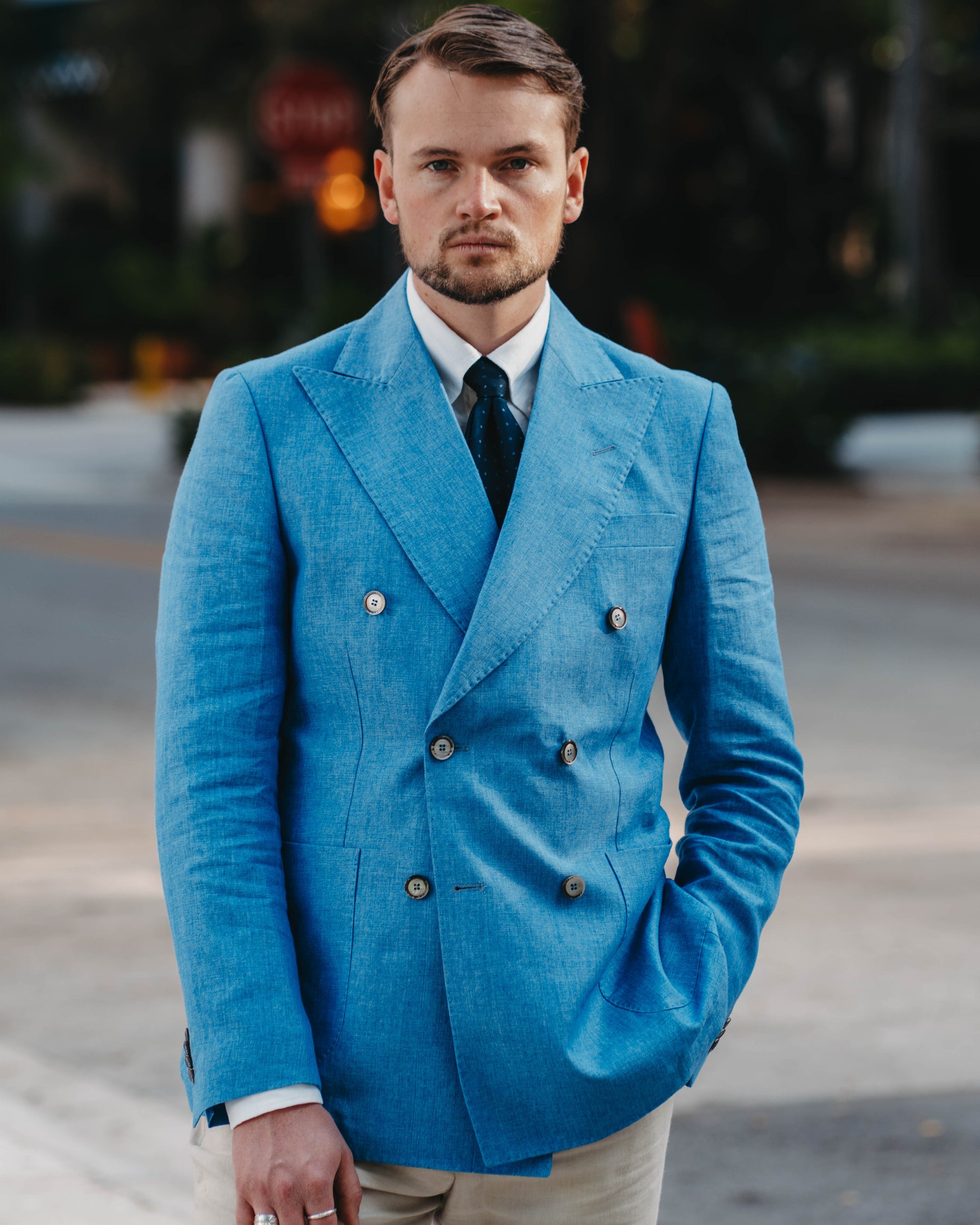 Man wearing a blue double-breasted jacket and beige pants standing outdoors.