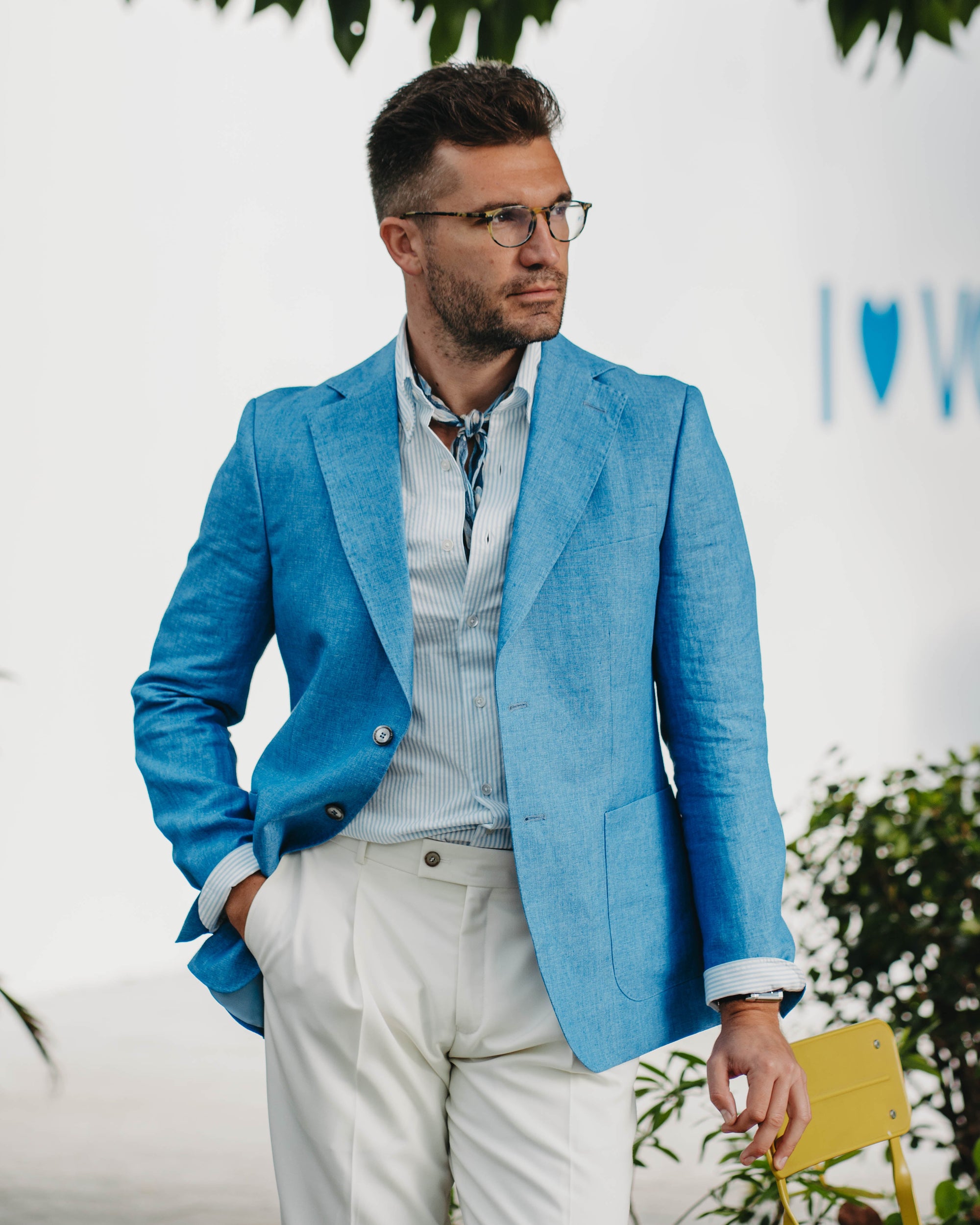 Man wearing a blue blazer and white pants standing outdoors with a blurred background