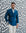 Man wearing a blue blazer and white pants standing against a patterned wall.
