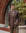 Man wearing a brown blazer and beige pants standing in front of a brick wall and plants.