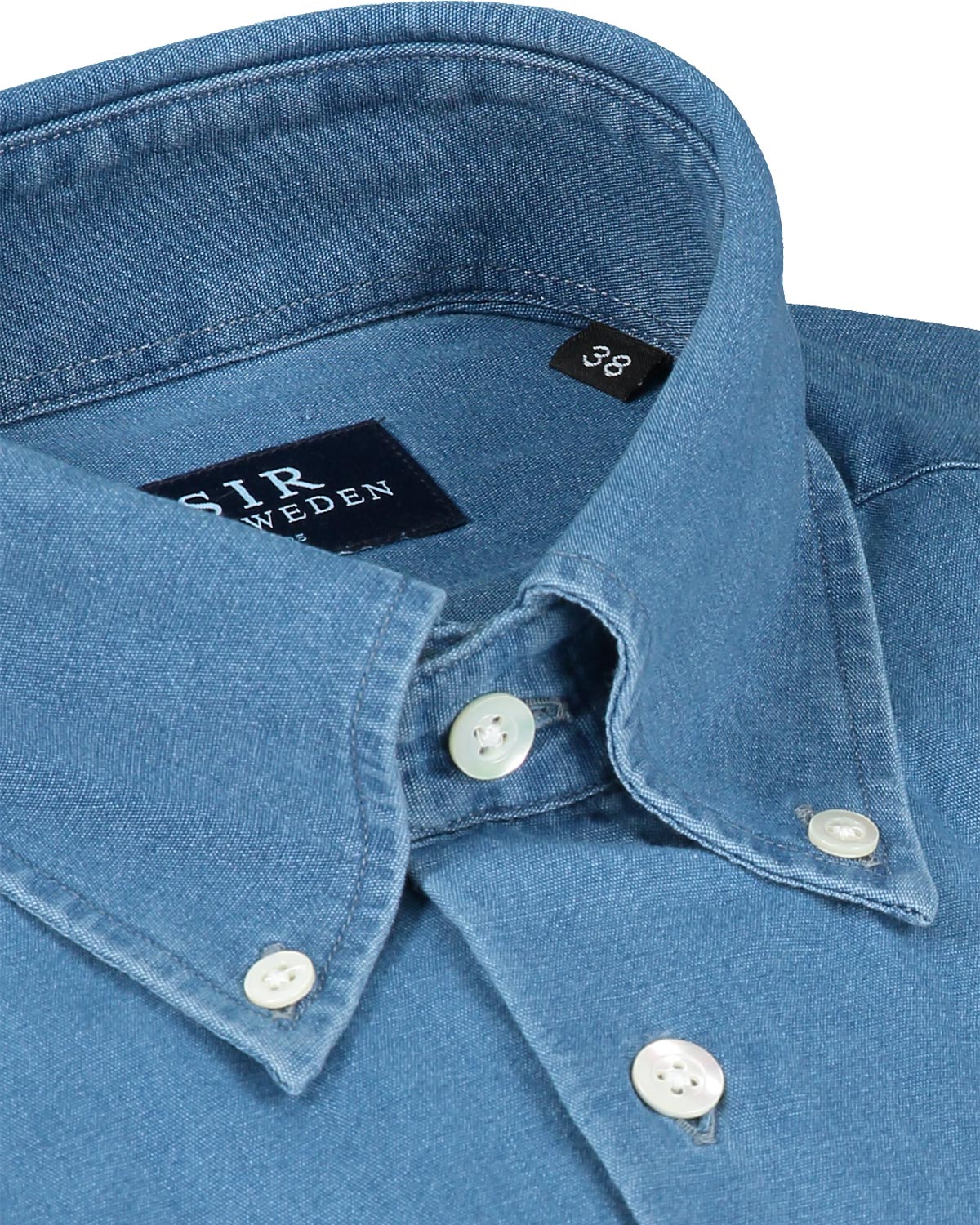Close-up of a blue denim shirt with a button down collar and brand label on a white background