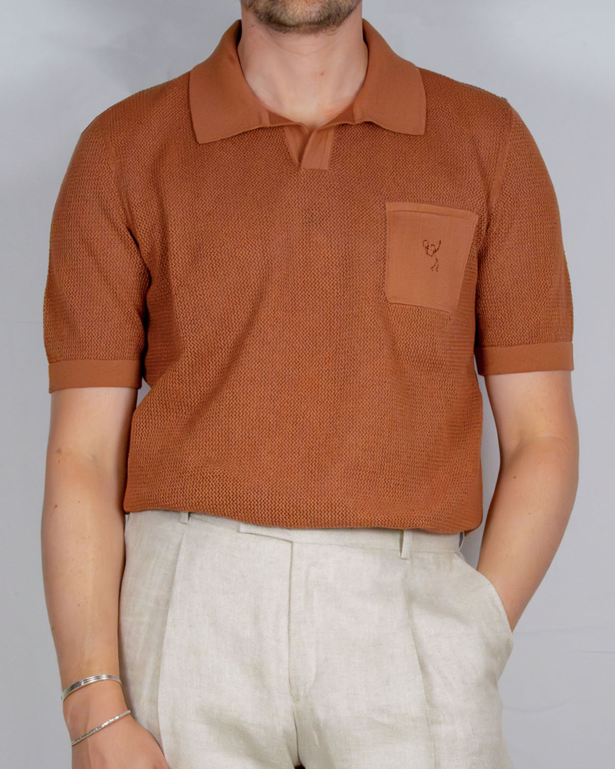 Person wearing a brown polo shirt with a logo of a stick figure playing tennis on a plain background