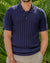 Man wearing a navy ribbed polo shirt against a green leafy background