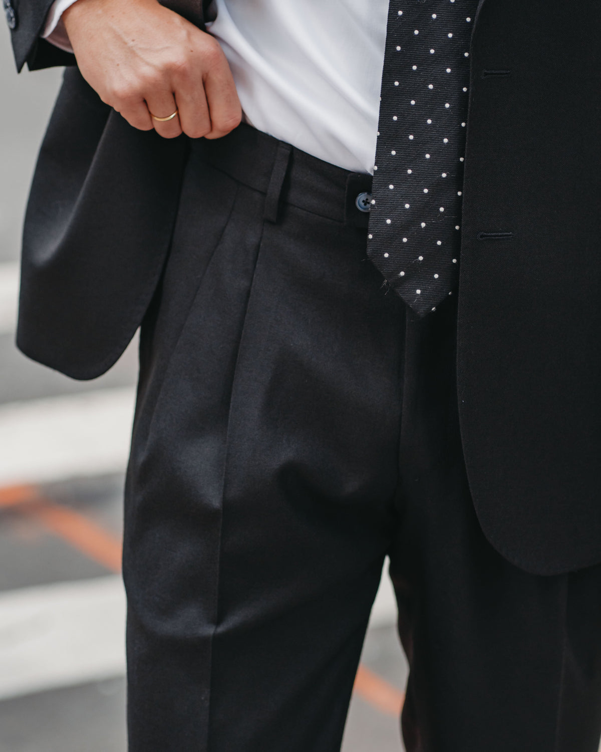 Close-up of a man wearing a black suit, white dress shirt, and a black tie with small white polka dots.