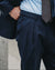 Close-up of a man wearing navy blue dress pants, a light blue dress shirt, and a brown patterned tie, with his hand in his pocket.
