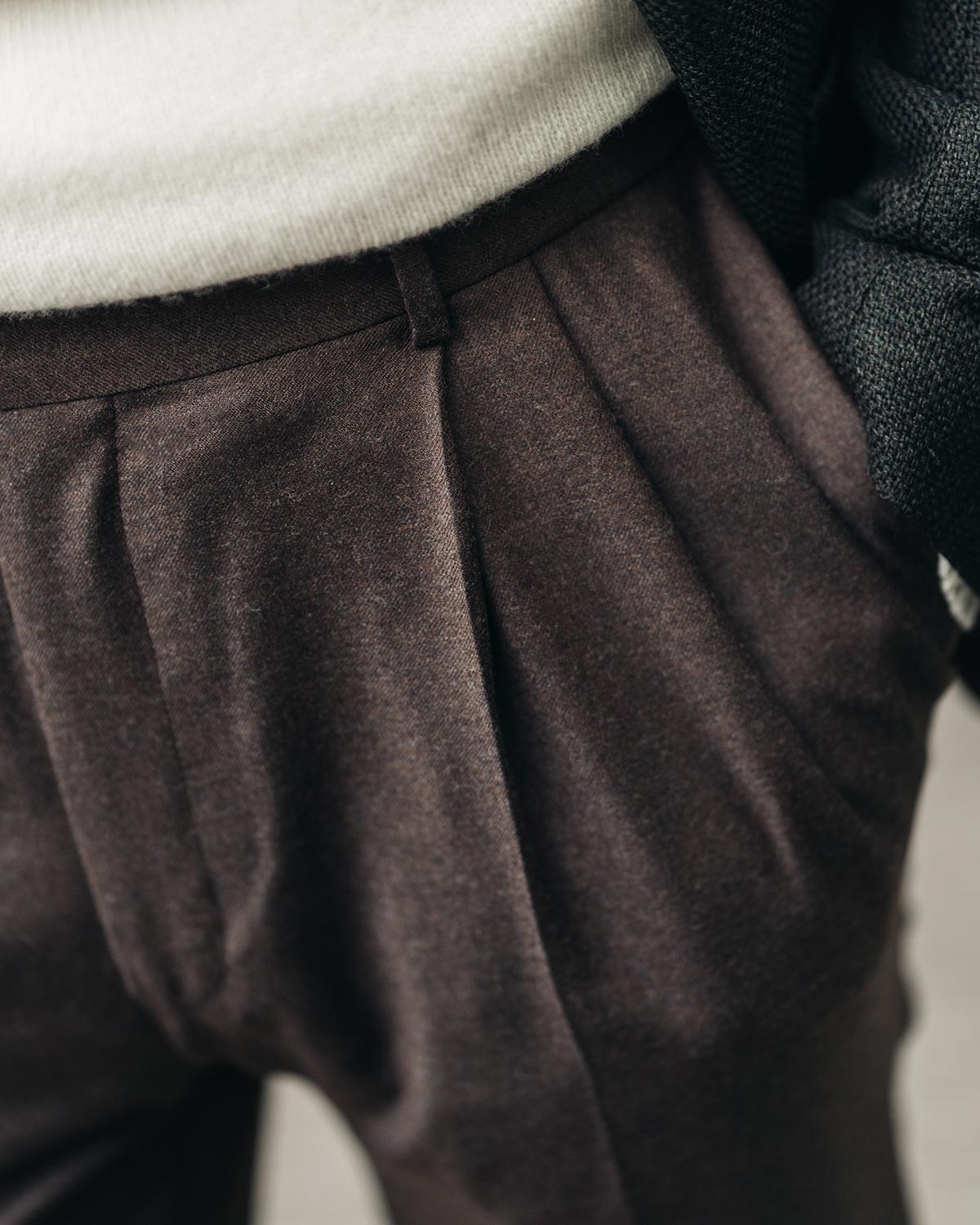 Close-up of brown pleated pants with a neutral background