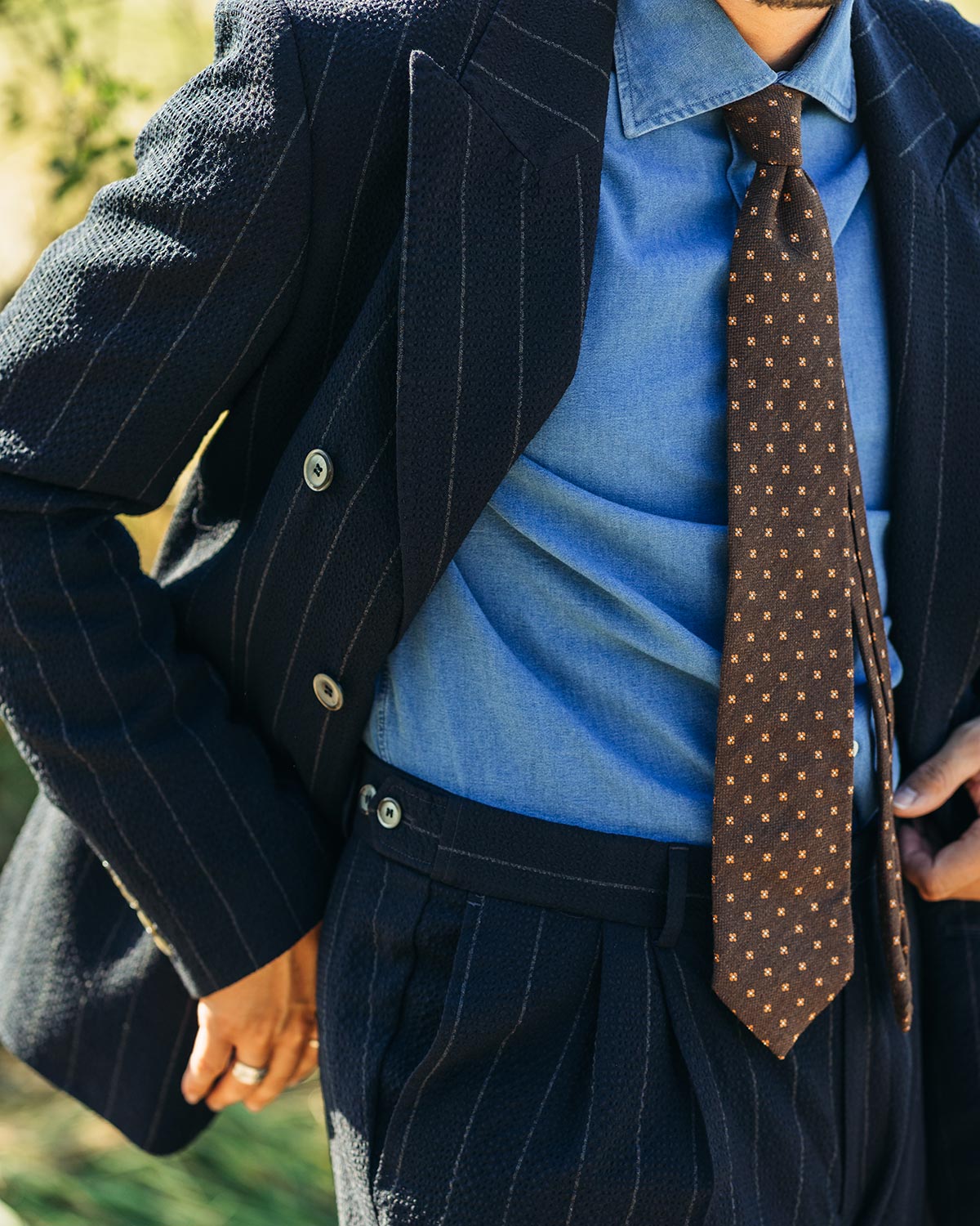 Person wearing a navy pinstripe suit with a blue denim shirt and brown patterned tie.