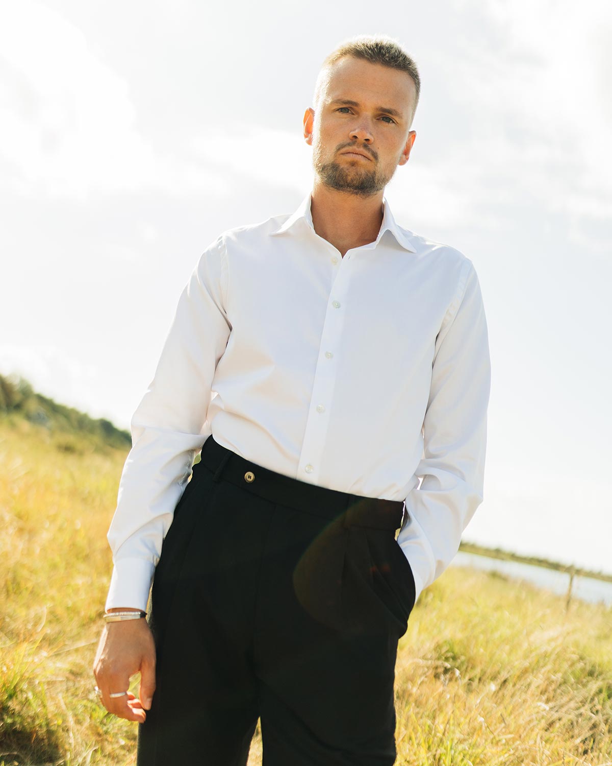 Man wearing a white shirt and black pants standing in a field with a blurred background