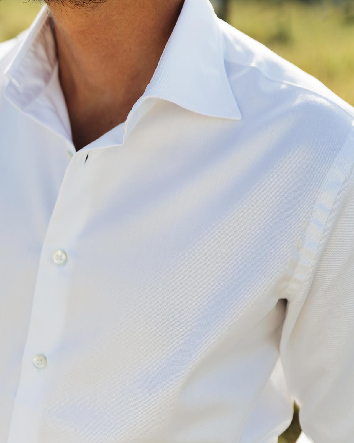 Close-up of a person wearing a white shirt with a blurred natural background