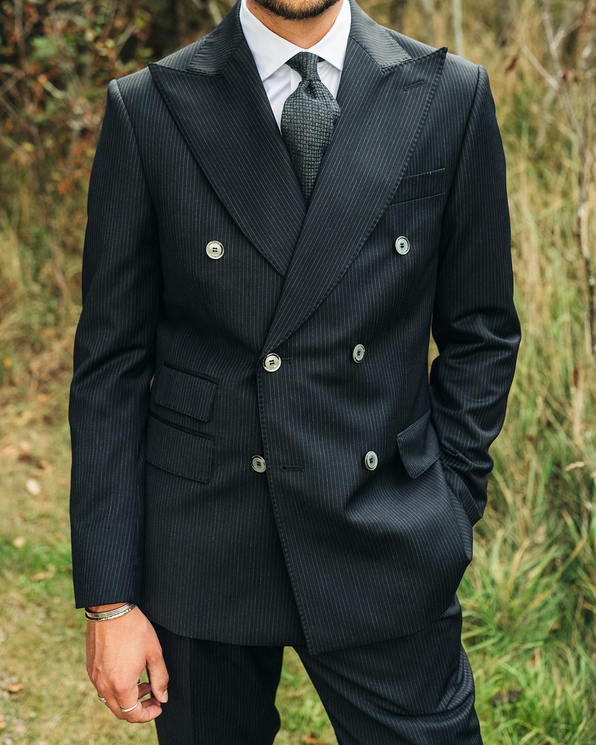 Black pinstripe suit with a tie against a natural background