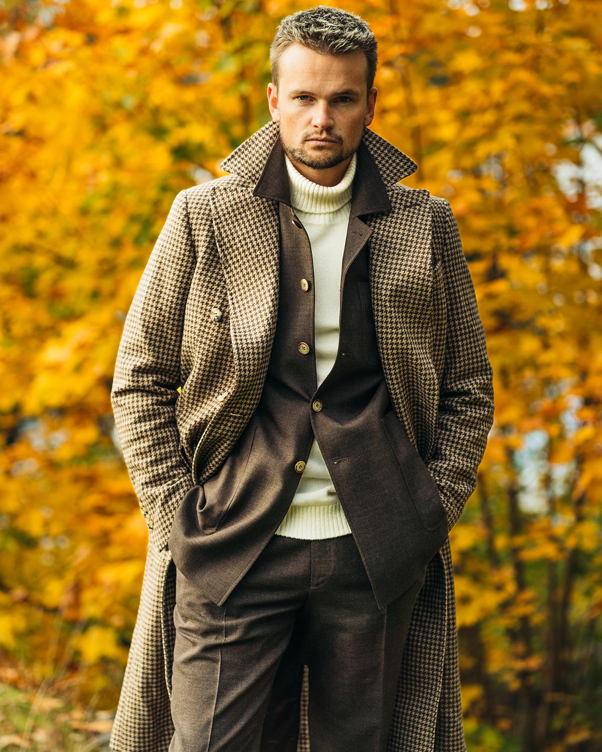 Man wearing a long coat in an autumn setting with yellow leaves.
