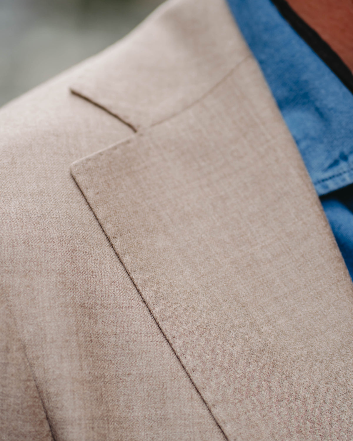 Close-up of a beige textured blazer lapel and shoulder over a blue collared shirt.