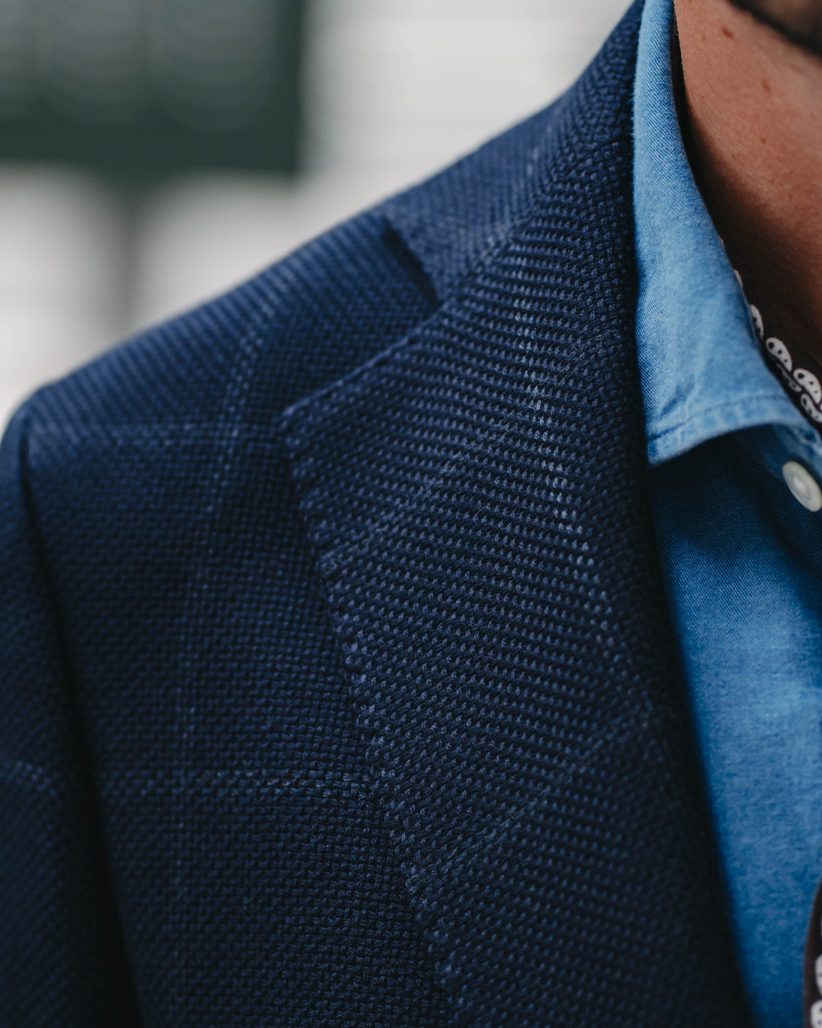 Close-up of a textured navy blue blazer worn over a light blue button-down shirt.