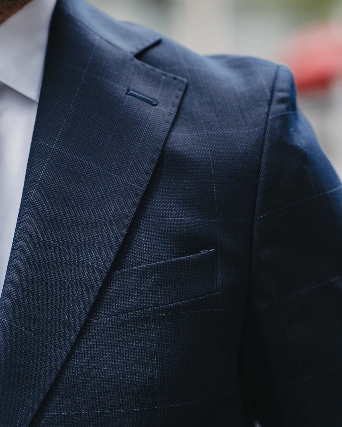 Close-up of a man wearing a navy blue windowpane plaid suit jacket over a white dress shirt.