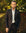 Man in a brown flannel suit standing outdoors with greenery in the background
