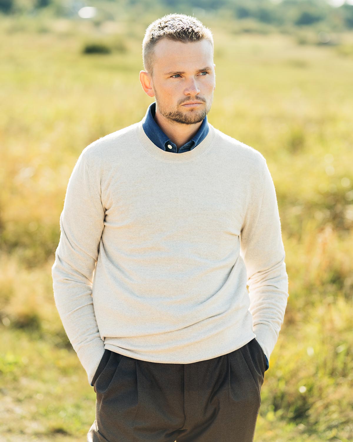 Man wearing a light-colored sweater and dark pants standing in a field