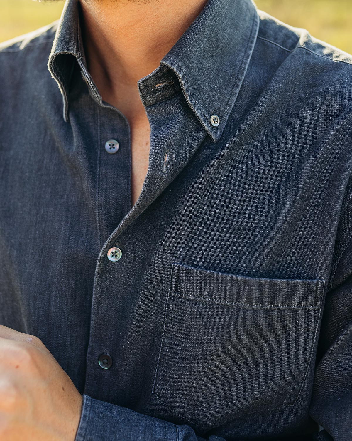 Close-up of a person wearing a dark denim shirt with a blurred background