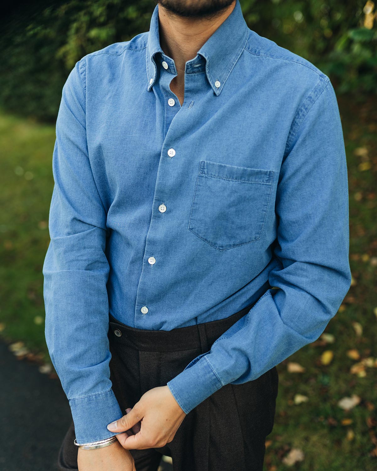 Person wearing a blue denim shirt with button down collar on a blurred natural background