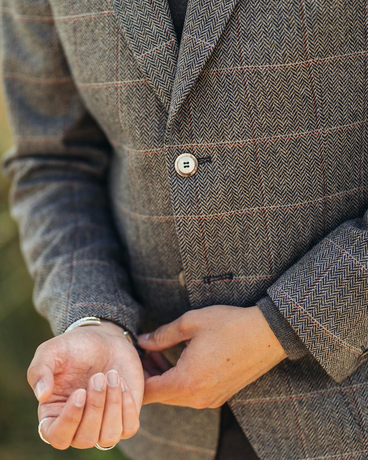 Close-up of a person wearing a textured brown jacket with hands clasped together.