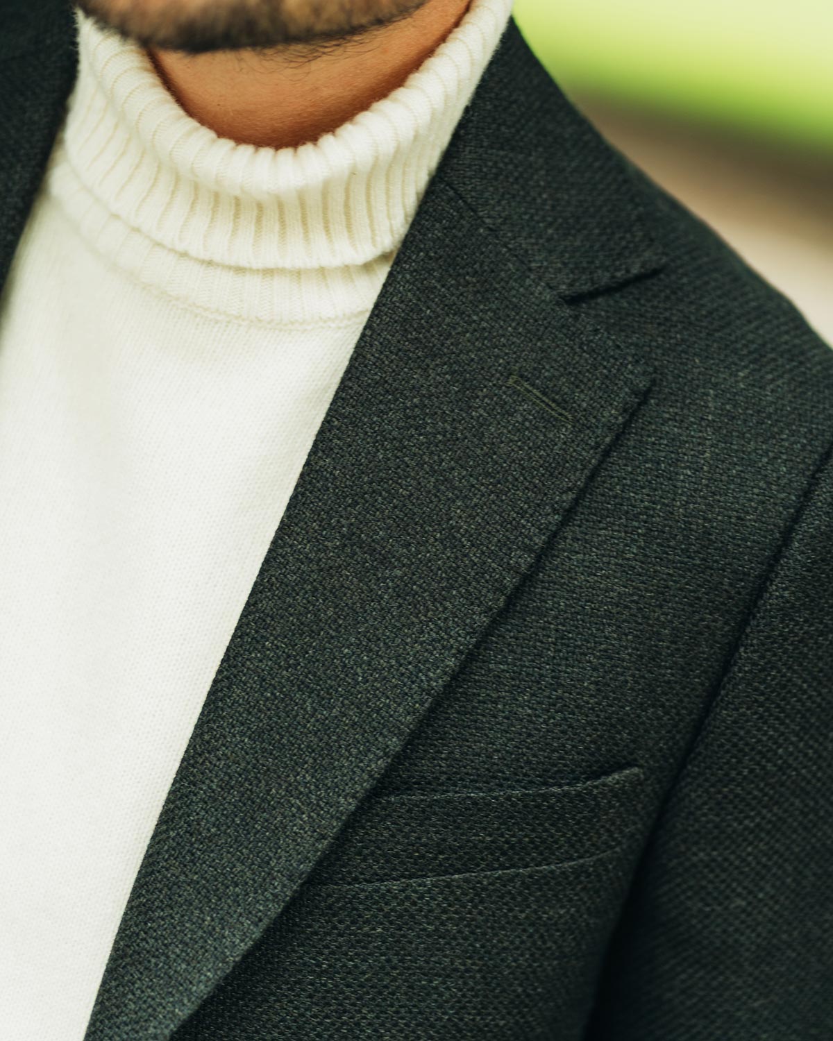 Green blazer over a white turtleneck sweater with a blurred background