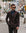 A man wearing a dark brown double-breasted suit, blue dress shirt, and dark tie walks down a city street wearing sunglasses.