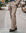 A man wearing a beige suit with a blue button-down shirt and dark brown leather shoes, standing on a city street.