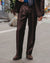 A man wearing a dark brown suit with a blue shirt, a gray patterned tie, and brown suede shoes, standing on a city street.