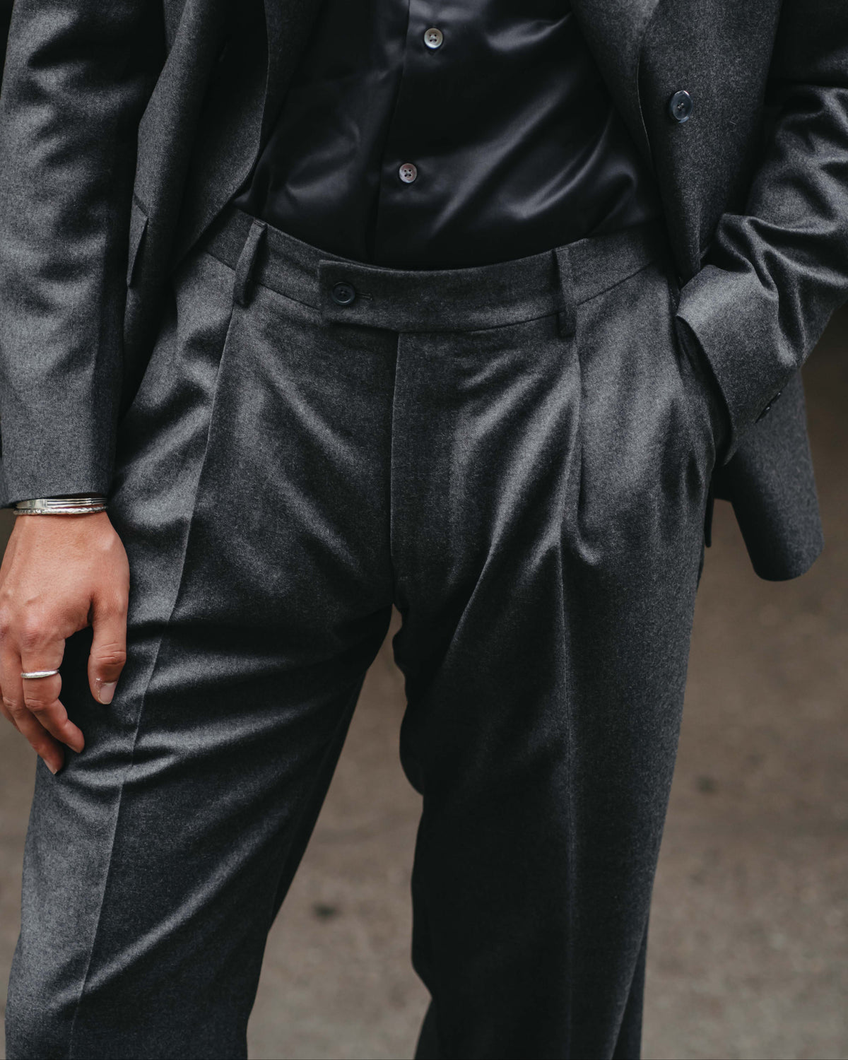 A close-up of a person wearing a dark charcoal gray two-piece suit with a black shirt underneath.