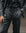 A close-up of a person wearing a dark charcoal gray two-piece suit with a black shirt underneath.