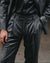 A close-up of a person wearing a dark charcoal gray two-piece suit with a black shirt underneath.