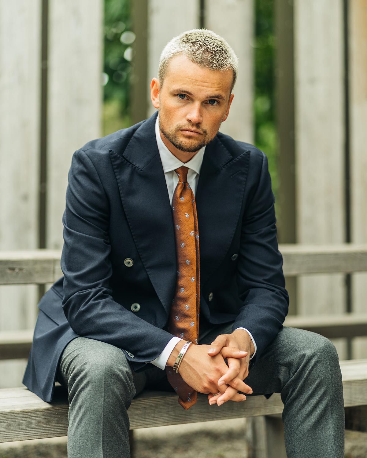 Man in a suit with a patterned tie sitting on a bench outdoors