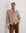 Man wearing a beige cardigan, white shirt, and brown pants with a red scarf against a white background