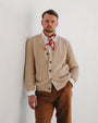 Man wearing a beige cardigan, white shirt, and brown pants with a red scarf against a white background